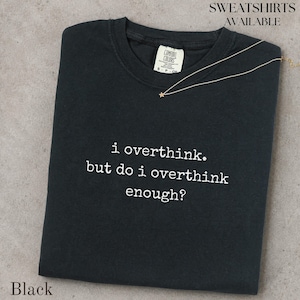 May include: A black crew neck t-shirt featuring white embroidered text that reads, i overthink. but do i overthink enough? The shirt has a white interior neck label with the brand name Comfort Colors and a size S P CH tag.
