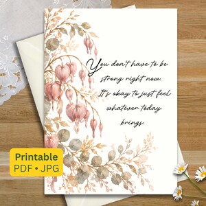 Op de afbeelding: Een rechthoekige wenskaart met een aquarelillustratie van roze gebroken hartjes en bladeren aan de linkerkant. De tekst luidt: You don't have to be strong right now. It's okay to just feel whatever today brings.