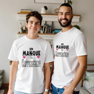 Könnte beinhalten: Zwei weiße T-Shirts mit dem französischen Text "EN MANQUE DE RAFFINEMENT" in Schwarz, mit rosa Herzakzenten. Die Shirts sind kurzärmlig und werden von zwei Personen getragen.