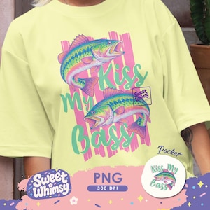 May include: Light yellow t-shirt with a graphic of two colorful bass fish and the text "Kiss My Bass." The design includes pink and green accents. A small round sticker with the same design is also visible.
