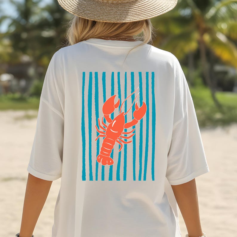 May include: A white short-sleeved t-shirt featuring a graphic on the back. The design consists of a bright orange lobster centered over a background of vertical teal blue stripes. The shirt is worn with a straw hat, visible from the back view.