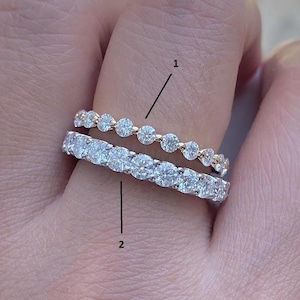 Könnte beinhalten: Zwei Diamantringe werden auf einem Finger gezeigt. Der obere Ring hat kleine, gleichmäßig verteilte Diamanten in einem Goldband. Der untere Ring hat eine durchgehende Reihe größerer Diamanten in einem Silberband.