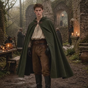 May include: A dark green hooded cloak worn over a beige long-sleeved shirt, brown trousers, and a wide brown leather belt. The outfit includes black gloves and black boots, with the cloak fastened at the neck by a metal clasp over a stone setting.