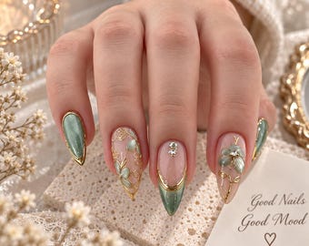 May include: Almond-shaped nails featuring a sage green and clear base with gold filigree accents, small rhinestones, and a floral design. One nail displays a solid sage green finish with a gold border, while others show intricate gold wire art.
