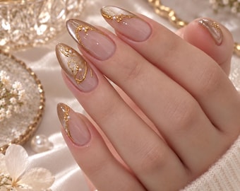 May include: Almond-shaped nails featuring a nude base coat with metallic gold filigree accents and small white pearls. The design includes intricate gold lines and delicate embellishments applied to the tips and sides of each fingernail.