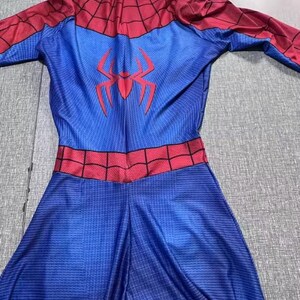 May include: A blue and red Spider-Man costume. The costume has a blue body with a red spider emblem on the back and red detailing on the shoulders and waist. It features a hood and long sleeves.