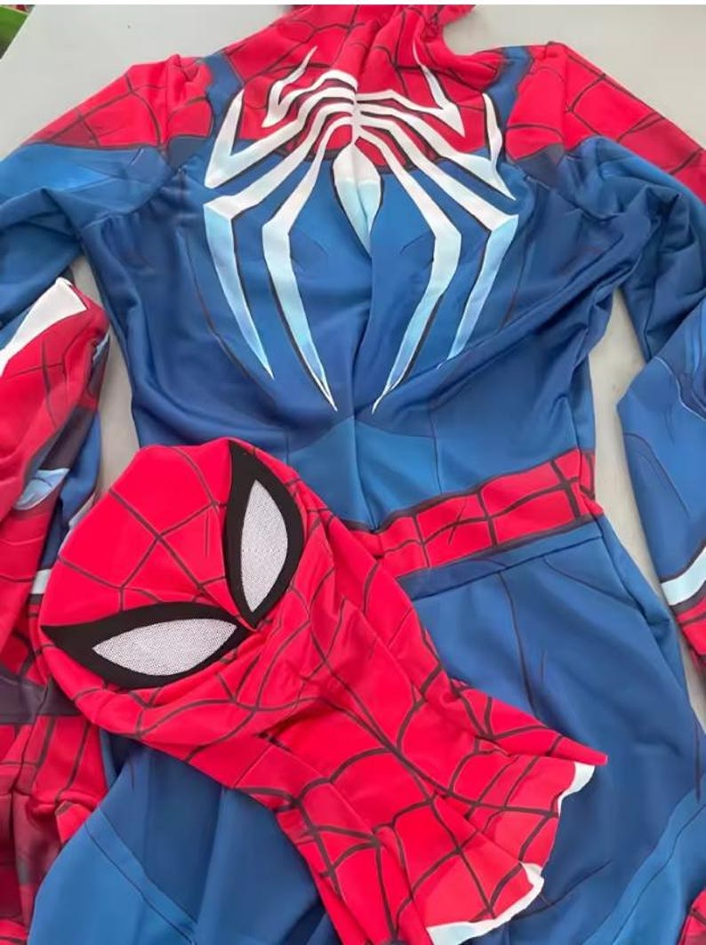 May include: A blue and red Spider-Man costume with a matching mask. The costume features a spider web design on the red areas and a large white spider emblem on the back. The mask has white eye shapes.