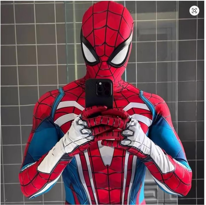May include: A red and blue Spider-Man costume with white accents, including a full head mask and gloves. The costume is being held up by a black phone. The suit has a web-like pattern.