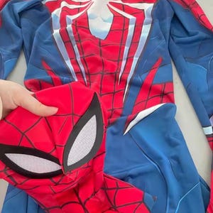 May include: A red and blue Spider-Man costume with a matching mask. The costume features a white spider emblem on the back and a web pattern design. The mask has white eye coverings.