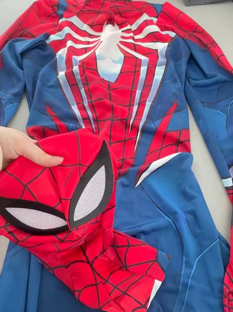 May include: A red and blue Spider-Man costume with a matching mask. The costume features a white spider emblem on the back and a web pattern design. The mask has white eye coverings.