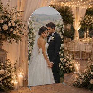 May include: An arched display stand featuring a printed photograph of a couple in wedding attire standing together. The bride wears a white strapless gown with a veil, and the groom wears a black suit. The stand has a metal frame base.