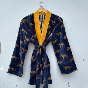 May include: A navy blue velvet robe featuring a repeating gold leopard print pattern. The garment includes a wide mustard yellow collar, long sleeves, and a matching tie belt at the waist. The interior lining displays a vertical black and white stripe.