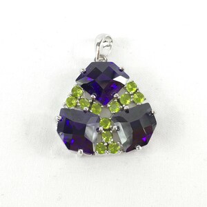 May include: A silver pendant with a geometric design featuring three large, faceted, purple amethysts surrounded by smaller, green peridot stones.