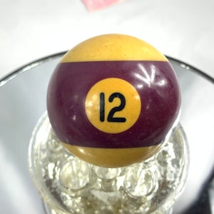 May include: A yellow and burgundy billiard ball with the number 12 printed in black on a yellow circle.