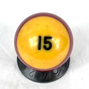 May include: A yellow billiard ball with a maroon band around the equator. The number 15 is printed in black on the ball.