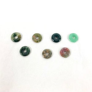 May include: Seven round, flat, green, black, and pink stone beads with a hole in the centre. The beads are arranged in a semi-circle on a white surface.