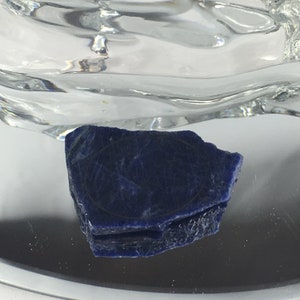 May include: A dark blue, rough-hewn piece of lapis lazuli with a circular pattern on the surface.