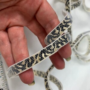 May include: White and black patterned trim with gold accents. The trim is made of a delicate mesh fabric.