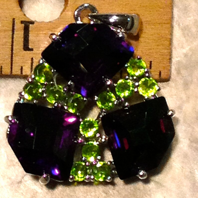 May include: A silver pendant with a geometric design featuring dark purple and light green gemstones.