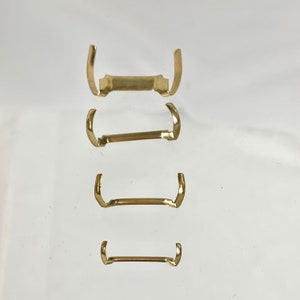 May include: Four gold-colored metal clasps of varying sizes. The clasps are shaped like a U with a straight bar connecting the two ends.