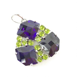 May include: A silver pendant with a cluster of purple and green square-shaped gemstones. The pendant has a loop at the top for attaching to a chain.