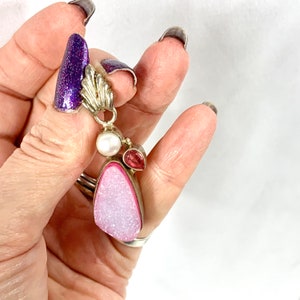 May include: A silver pendant with a pink and white agate stone, a pearl, and two pink stones. The pendant is hanging from a silver chain.