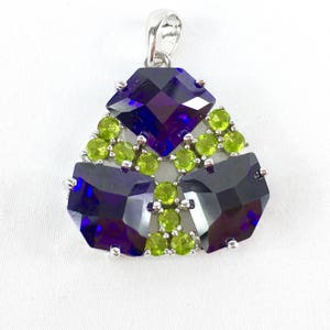 May include: A silver pendant with a geometric design featuring three large, faceted, dark purple gemstones surrounded by smaller, light green gemstones.