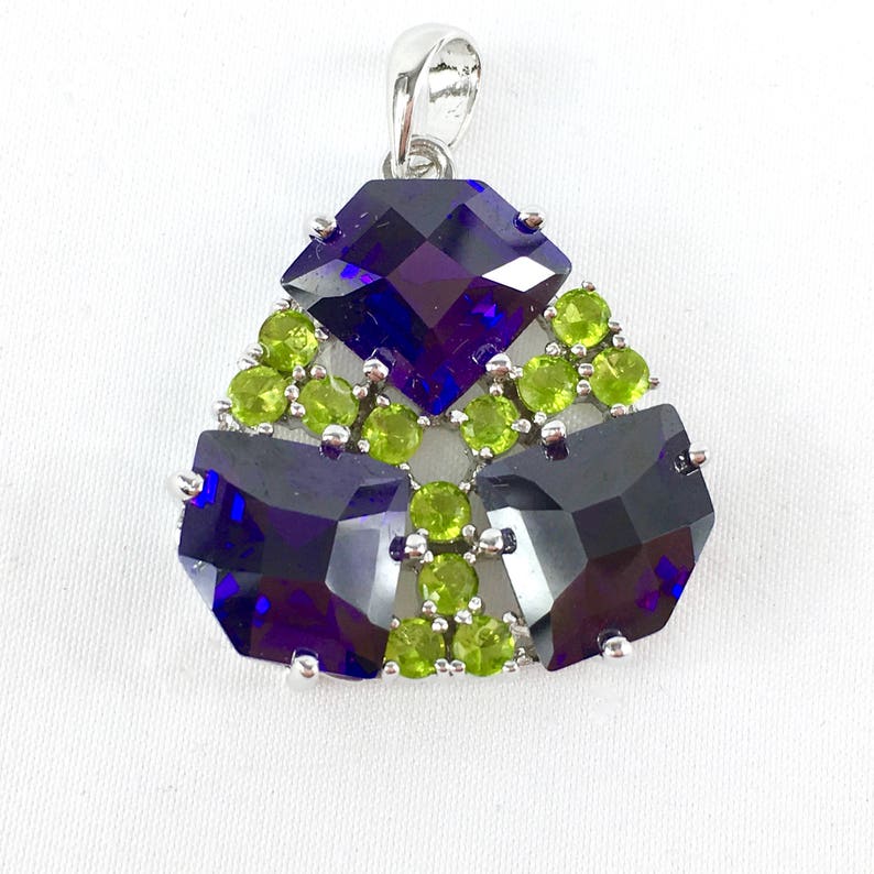 May include: A silver pendant with a geometric design featuring three large, faceted, dark purple gemstones surrounded by smaller, light green gemstones.