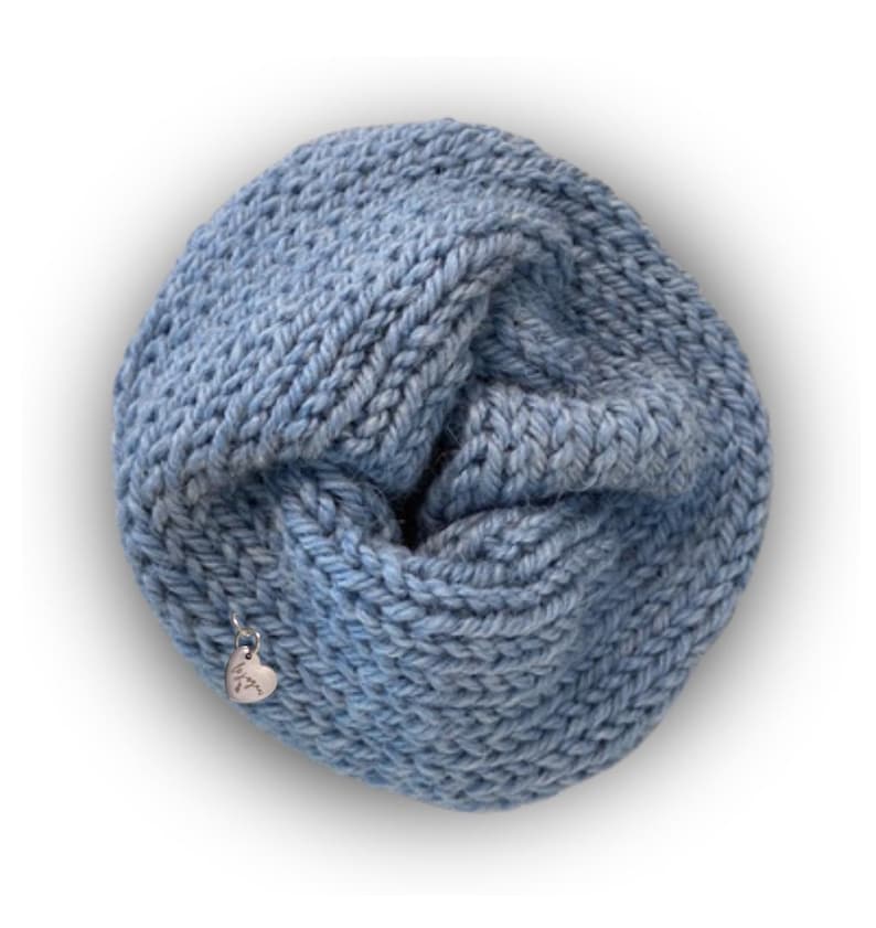 May include: A light blue infinity scarf made of thick, chunky knit yarn. The circular scarf features a textured, braided stitch pattern and includes a small, silver-toned heart-shaped metal charm attached to the side with the word "love" engraved.