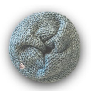 May include: A light blue infinity scarf made of thick, chunky knit yarn. The circular scarf features a small, silver-toned heart-shaped charm attached to the fabric, which is engraved with the cursive text "love you" on its surface.
