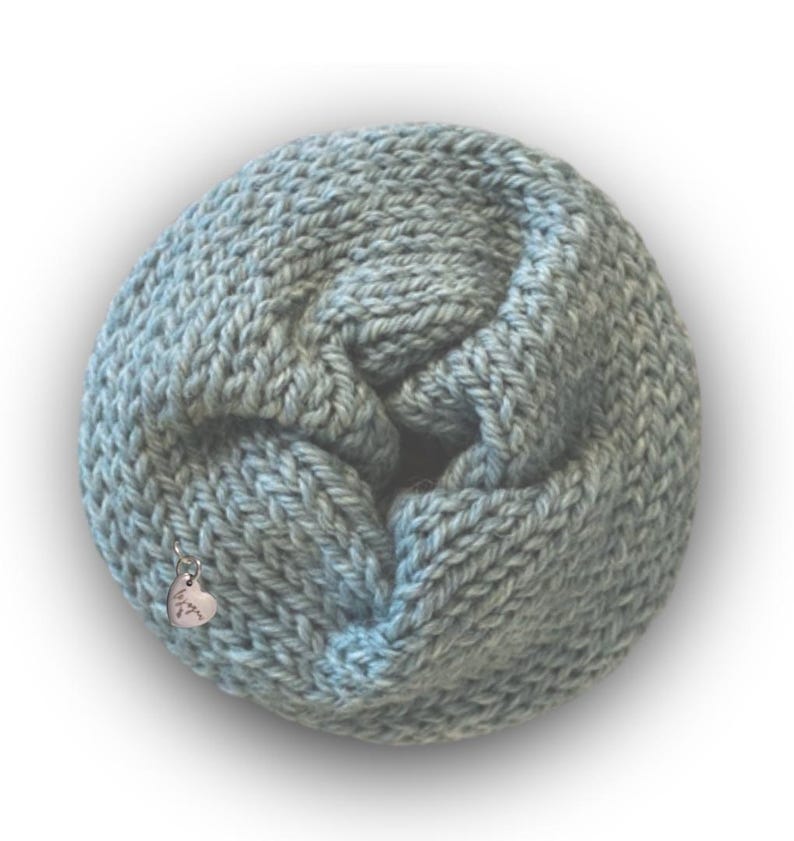 May include: A light blue infinity scarf made of thick, chunky knit yarn. The circular scarf features a small, silver-toned heart-shaped charm attached to the fabric, which is engraved with the cursive text "love you" on its surface.