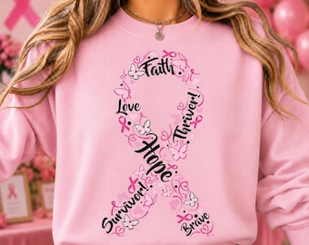 May include: A light pink long-sleeve sweatshirt featuring a large breast cancer awareness ribbon graphic in black. The ribbon design incorporates the words Faith, Love, Hope, Survivor, Thriver, and Brave, along with small butterfly and heart icons.