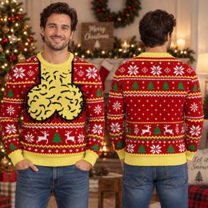May include: A red and yellow long-sleeve knit jumper featuring a graphic of two yellow rounded shapes on the front. The jumper has a crew neckline and a festive pattern of white snowflakes, green Christmas trees, and white reindeer.