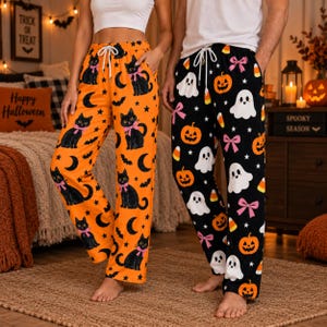 May include: Two pairs of lounge pants with Halloween themes. One pair is orange with a black cat, crescent moon, and bat pattern. The other pair is black with a white ghost, orange pumpkin, and pink bow pattern. Both feature white drawstrings.