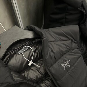 May include: Black quilted down jacket with a shiny interior. The jacket features a zipper closure and a small logo on the chest. The jacket is hanging on a black hanger.
