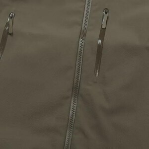 May include: Close-up of a khaki jacket featuring a central zip and three vertical zipped pockets. The zips have silver pulls. The fabric looks smooth and water-resistant, suitable for outdoor wear.