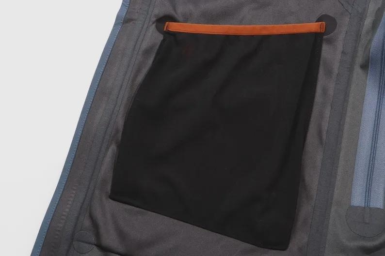 May include: Detail of a grey jacket interior, showing a large black pocket with a brown trim. The jacket has blue edging and a zip detail.