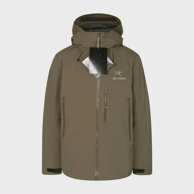 May include: A khaki-coloured hooded jacket with a zip closure and multiple pockets. The jacket has a brand logo on the chest and a tag attached to the zip. The jacket is designed for outdoor activities.