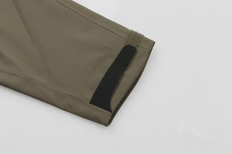 May include: Detail of olive-green fabric, possibly a sleeve. A black stripe and velcro fastening are visible. The material is smooth and likely durable. The image is set against a plain white background.