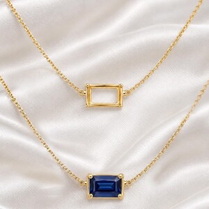 Peut inclure: Un ensemble de colliers superposés en or composé de deux chaînes délicates. La chaîne supérieure présente un pendentif cadre rectangulaire en or, tandis que la chaîne inférieure porte une pierre bleue rectangulaire sertie en or.