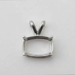 May include: A silver-toned metal pendant setting featuring a rectangular frame with rounded corners and four small prongs at each corner. The setting includes a V-shaped bail at the top for attachment, designed to hold a gemstone securely in place.