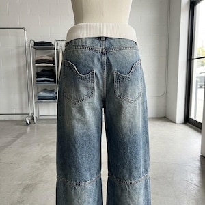 May include: Light blue denim jeans with a wide leg design. The jeans have a faded wash and feature large back pockets. The waistband is paired with a white ribbed knit top. The jeans are displayed on a mannequin.