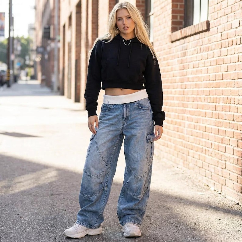 May include: A black cropped hoodie with a drawstring neckline and long sleeves. The hoodie is paired with light blue denim cargo pants with multiple pockets and a relaxed fit. White sneakers complete the casual outfit.