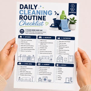 May include: A white checklist titled "DAILY CLEANING ROUTINE" with blue and green accents. The checklist is divided into sections for the kitchen, bedroom, bathroom, living area, laundry, and weekly tasks. A hand is holding the checklist.