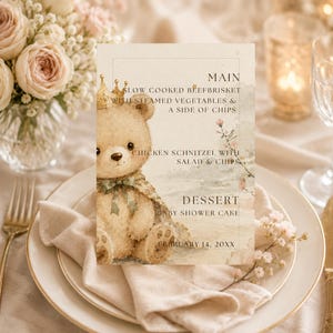 Peut inclure: Une carte de menu rectangulaire avec une illustration à l'aquarelle d'un ours en peluche portant une couronne dorée et un nœud vert. Le texte indique : MAIN SLOW COOKED BEEFBRISKET WITH STEAMED VEGETABLES & A SIDE OF CHIPS, CHICKEN SCHNITZEL WITH SALAD & CHIPS, DESSERT BABY SHOWER CAKE FEBRUARY 14, 20XX.