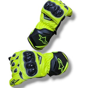 Könnte beinhalten: Zwei neongelbe und schwarze Motorradhandschuhe. Die Handschuhe haben eine schwarze Schutzpanzerung an Knöcheln und Handgelenk. Der Text "GPRO" ist auf dem Handgelenkbereich aufgedruckt. Ein Sternlogo ist sichtbar.