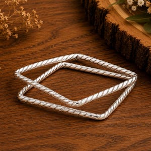 May include: Two square-shaped silver bangles featuring a twisted rope texture. The bracelets are crafted from a polished metallic material with a reflective finish, showcasing a consistent spiral pattern along the entire length of each square band.