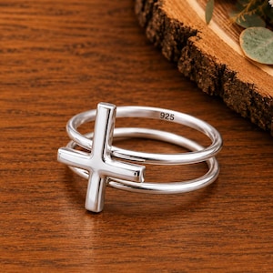 Peut inclure: Une bague en argent poli présentant un design à double anneau relié par une croix verticale. La surface intérieure de l'anneau porte clairement le poinçon 925, indiquant une composition en argent sterling. La bague a une finition lisse.