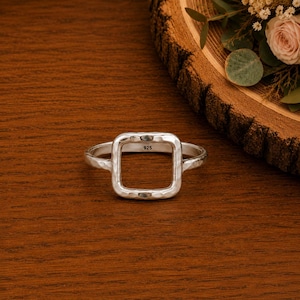 May include: A silver ring featuring a square-shaped centerpiece with a hammered, textured finish. The interior of the band is clearly stamped with the hallmark 925, indicating sterling silver composition. The ring has a polished, reflective surface.