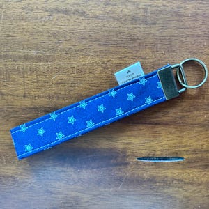 May include: A blue fabric keychain wristlet with a repeating pattern of light blue stars. The wristlet has a metal clasp and key ring. A small tag reads "Handmade with love".